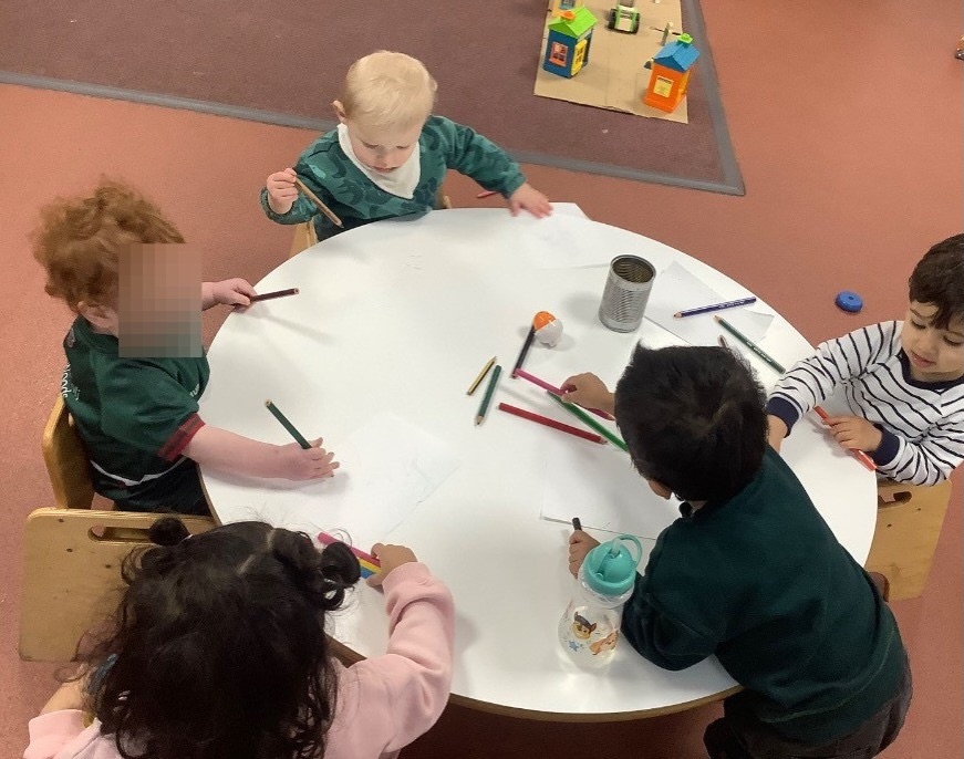 Five children seated around a low table, drawing together with coloured pencils