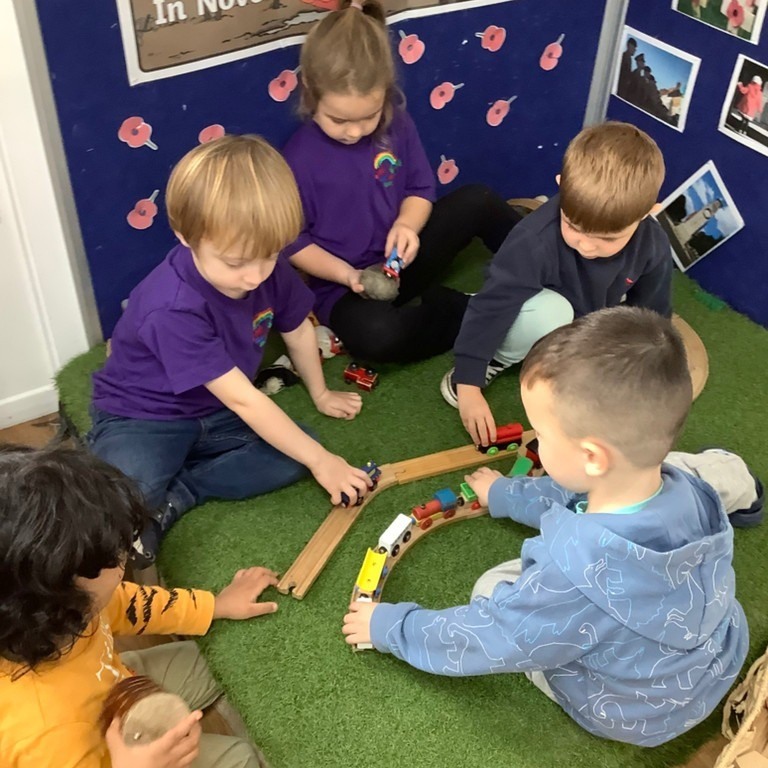 A group of children building a wooden train track together on the carpet of a primary school setting
