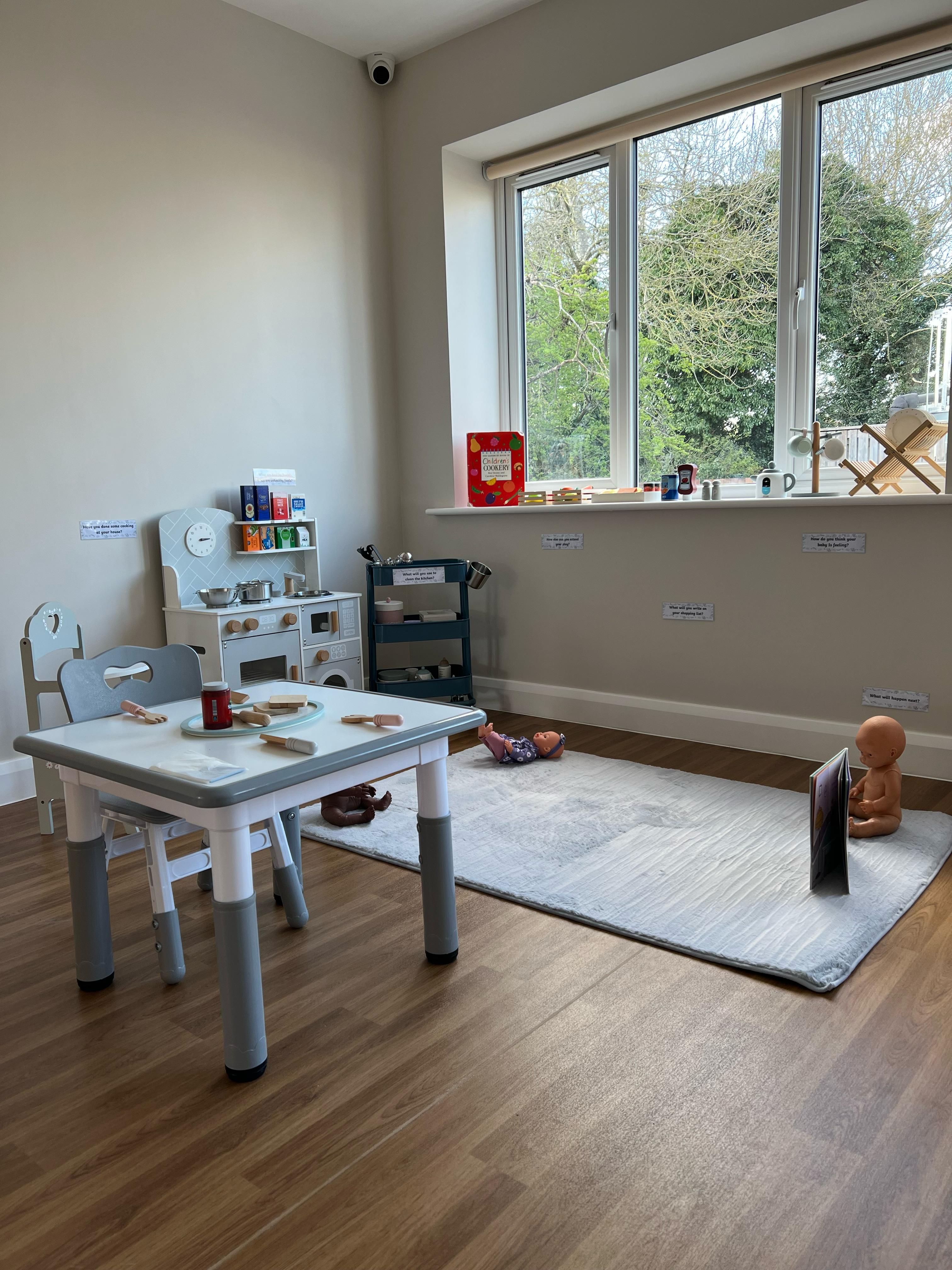 Light-filled preschool room at our Thurnby setting — wooden play kitchen, child-sized table, large window overlooking trees