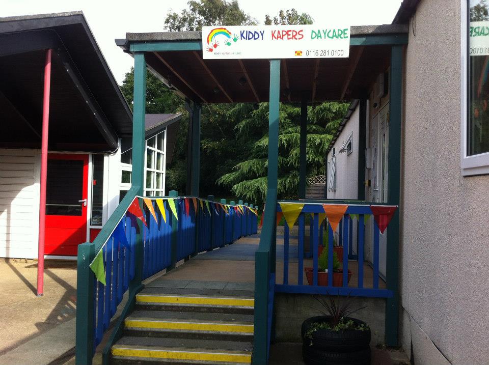 Kiddy Kapers Wigston entrance — covered walkway with colourful pennant bunting and the Kiddy Kapers Daycare signboard above the front door
